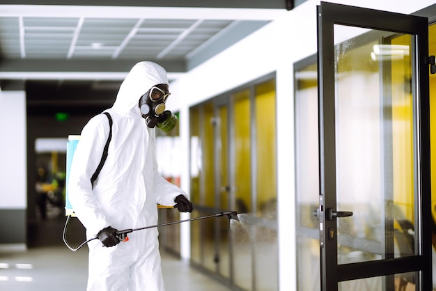 Desinfección de la oficina para prevenir COVID-19, Hombre con traje protector de materiales peligrosos con productos químicos en aerosol.