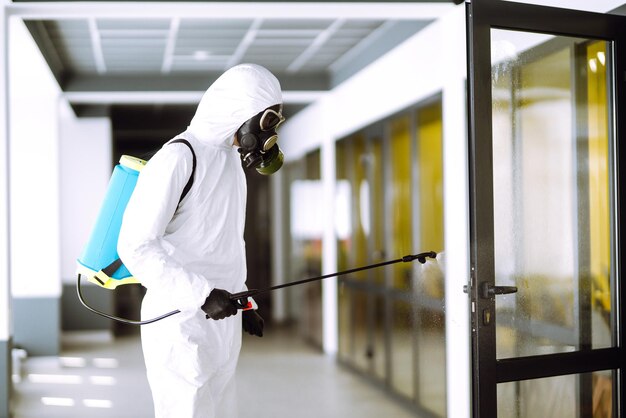 Desinfección de la oficina para prevenir COVID19 Hombre con traje protector de materiales peligrosos con productos químicos en aerosol