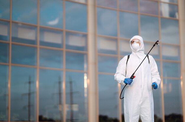 Desinfección para prevenir COVID-19, Hombre en traje protector de materiales peligrosos con spray.