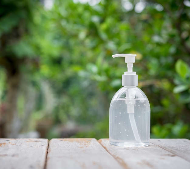 Desinfectante de manos blanco o botella de bomba de gel de alcohol en la parte superior de madera con naturalezas verdes