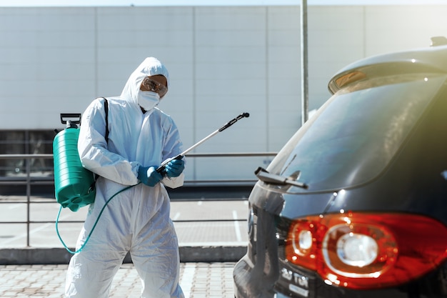 El desinfectante en un traje protector realiza la desinfección en el área contaminada del automóvil para prevenir el coronavirus. Cuidado de la salud.