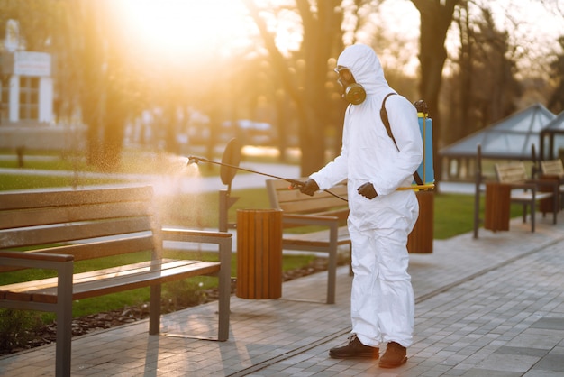 Desinfektionsbank des Mannes im Schutzanzug im öffentlichen Park in der Quarantänestadt. Infektionsprävention und Seuchenbekämpfung. Covid 19.