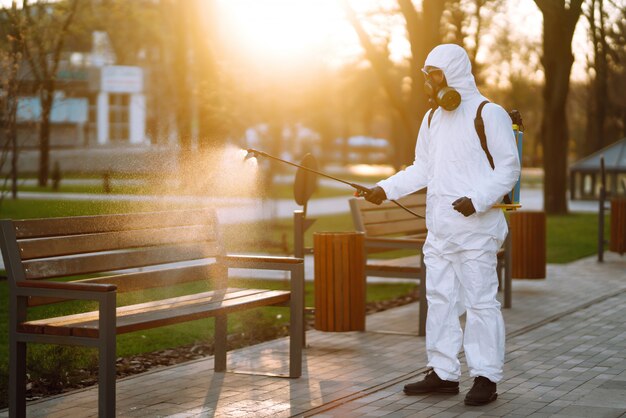 Desinfektionsbank des Mannes im Schutzanzug im öffentlichen Park in der Quarantänestadt. Infektionsprävention und Seuchenbekämpfung. Covid 19.