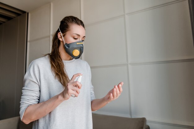 Foto desinfetante para as mãos mulher pulverização em casa usando máscara protectora