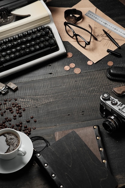 Desktop cinza escuro brutal masculino Sobre a mesa há uma máquina de escrever uma xícara de café e uma câmera um caderno desenha óculos um relógio de pulso uma caneta uma régua moedas e grãos de café estão espalhados