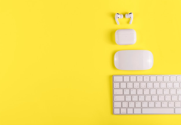 Desktop mit Tastatur, kabellosen Kopfhörern und Maus auf Farbe des Hintergrunds des Jahres 2021. Gelb leuchtend