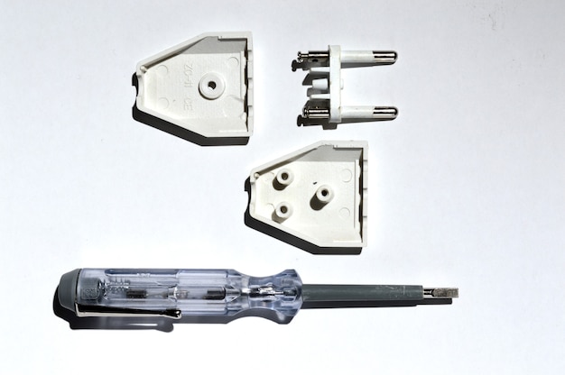 Desmontagem do plugue elétrico usando um testador de chave de fenda. no fundo branco