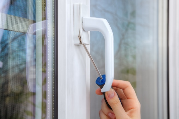 Desmontar la manija de la ventana de pvc con un destornillador, mano de cerca con la herramienta.