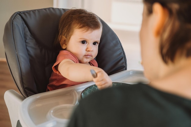 Desordenado sonriente niña comiendo con una cuchara en la silla alta nutrición orgánica natural alimentos orgánicos bab...