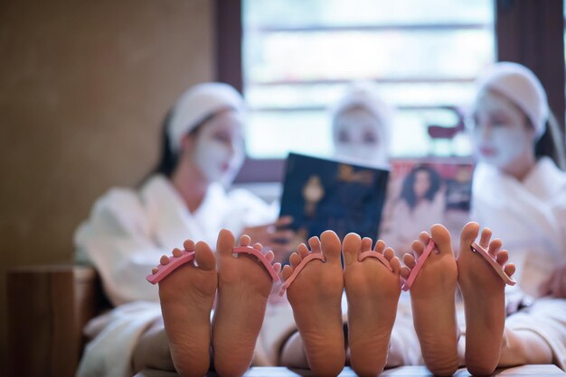 despedida de soltera en spa, chicas con revista de lectura de mascarillas, concepto de pedicura, pies con separador en foco