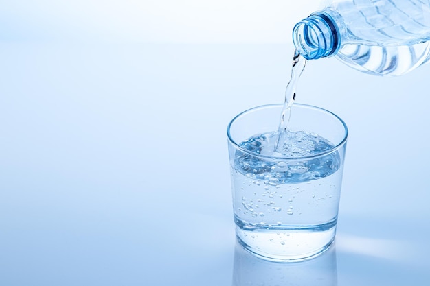 Despejando água da garrafa no copo isolado em fundo azul com espaço de cópia