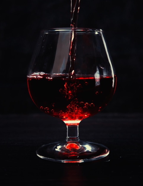 Despejando vinho tinto em um copo sobre um fundo escuro