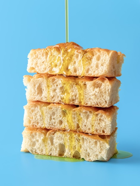 Despejar o azeite sobre o pão focaccia Focaccia fatiada sobre um fundo azul