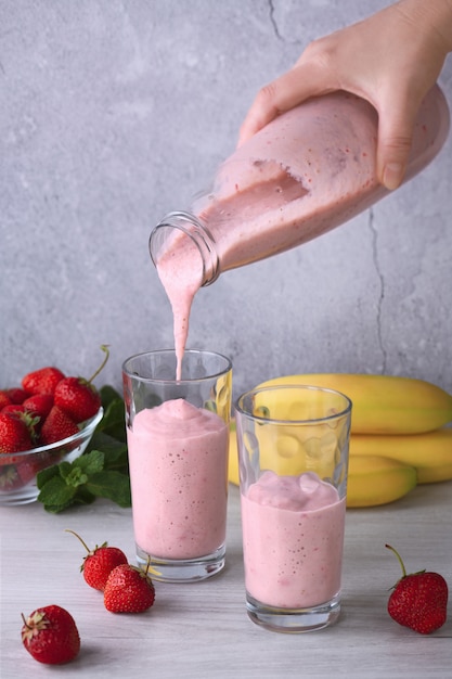 Despeje o smoothie de banana e morango recém-preparado de uma garrafa em copos