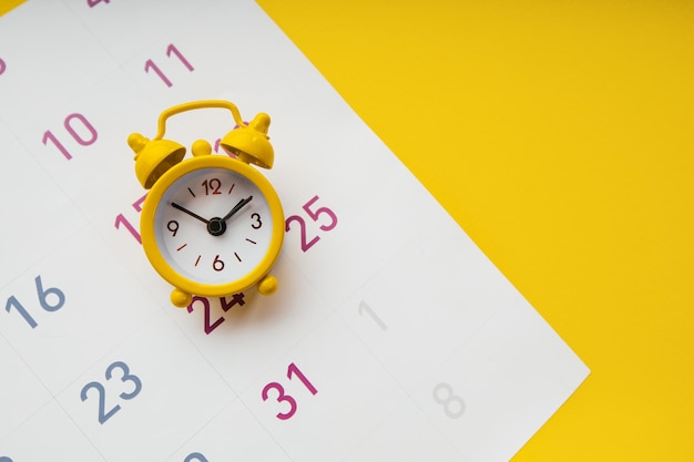 Foto despertador amarelo e calendário em um fundo amarelo closeup conceito de prazo