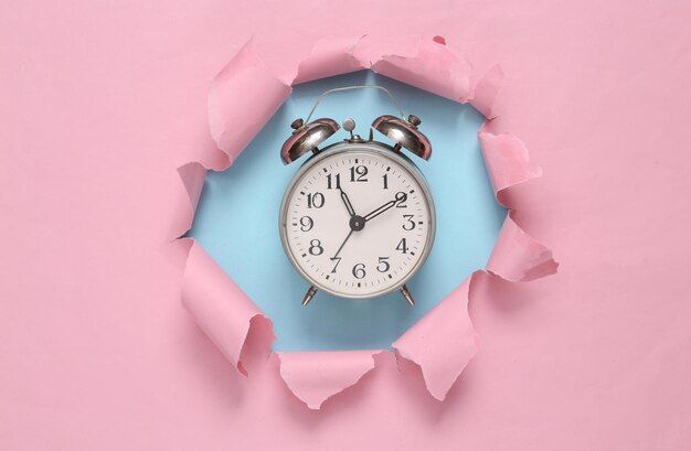 Despertador através de um buraco rasgado no fundo pastel azul-rosado Arte conceitual Tendência de cor pastel Minimalismo