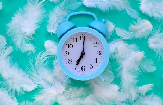 Despertador azul con plumas blancas sobre fondo verde con espacio para copiar. Madrugada