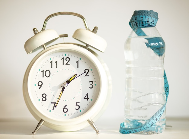 Despertador blanco con botella de agua, cinta métrica azul como concepto de dieta - sobre fondo blanco.