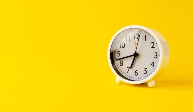 Despertador branco em um conceito de tempo de fundo amarelo com tempo de trabalho de palavras-chave
