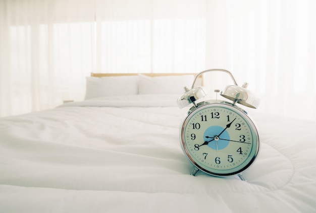 Despertador en la cama en el dormitorio por la mañana con luz solar.