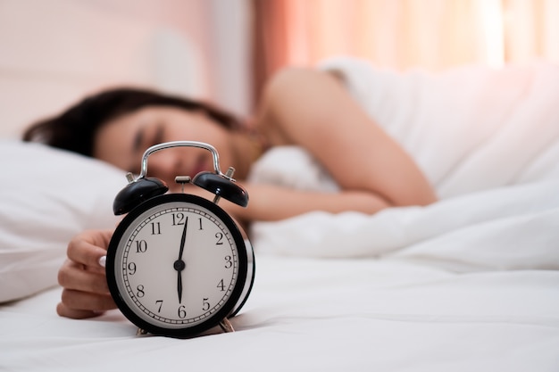 Despertador com a jovem mulher bonita que dorme pacificamente na cama branca no quarto.