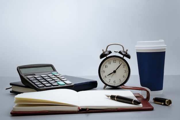 Despertador con cuaderno, calculadora, bolígrafo y taza de café sobre fondo gris