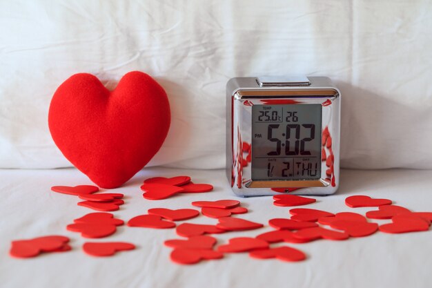 Despertador digital y forma de corazón en la sábana blanca contra la almohada, concepto de dormir bien