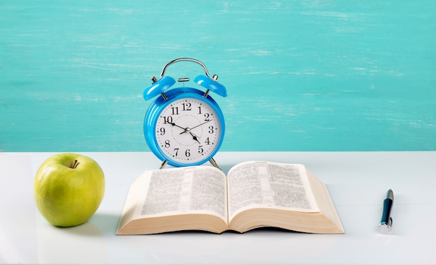 Despertador, libro, bolígrafo, manzana sobre la mesa.