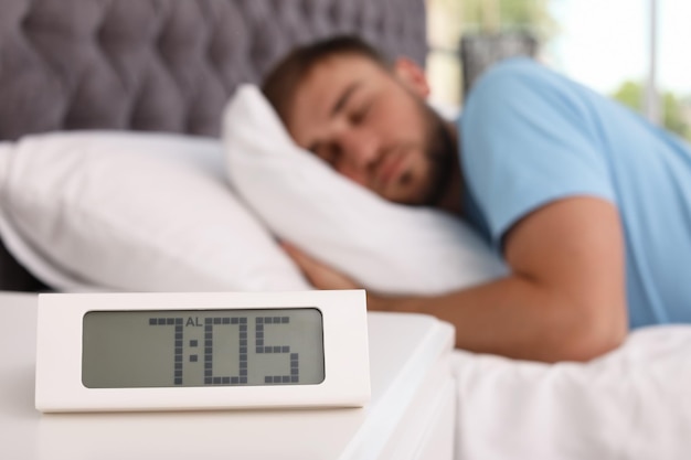 Despertador en la mesa y joven durmiendo en la cama en casa