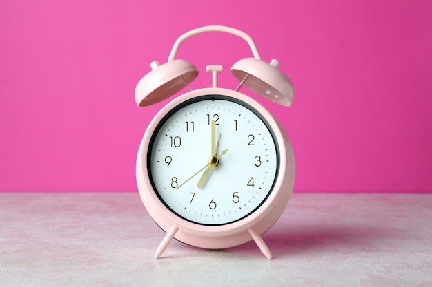 Despertador en la mesa con textura blanca sobre fondo rosa