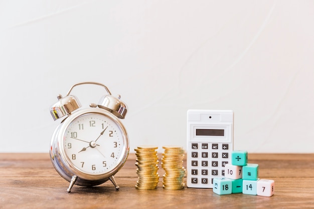 Foto despertador, monedas apiladas, calculadora y bloques de matemáticas en el escritorio de madera