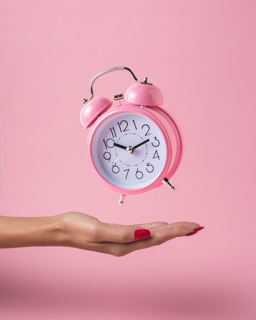 Despertador na mão de uma mulher isolado em rosa