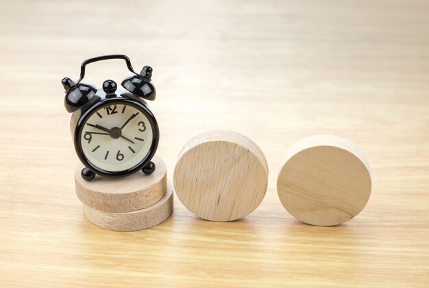 Despertador negro en la pila de pieza de madera redonda con pieza de madera en blanco en la mesa de luz de madera