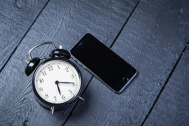 Despertador negro con teléfono celular en una mesa de madera