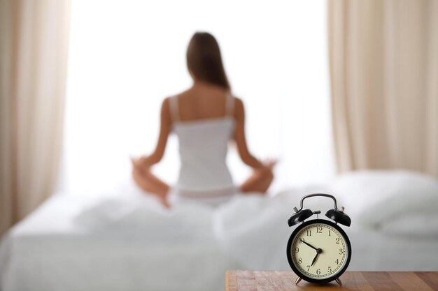 Despertador de pie en la mesita de noche ya ha sonado temprano en la mañana para despertar Mujer hacer yoga en la cama en el fondo Despertar temprano concepto de contemplación de estilo de vida saludable