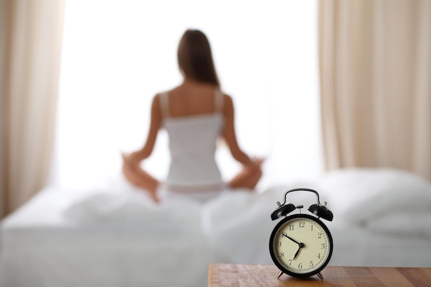 Despertador de pie en la mesita de noche ya ha sonado temprano en la mañana para despertar Mujer hacer yoga en la cama en el fondo Despertar temprano concepto de contemplación de estilo de vida saludable