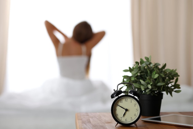 Foto el despertador de pie en la mesita de noche ya ha sonado temprano en la mañana para despertar a la mujer que se estira en la cama en el fondo despertar temprano sin dormir lo suficiente concepto de sueño excesivo