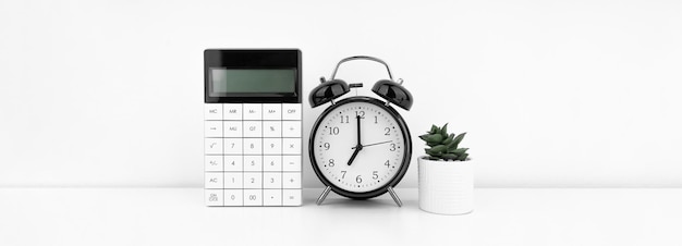 Despertador preto com calculadora contra uma parede branca Conceito financeiro
