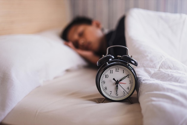 Despertador que muestra las 6 de la tarde con un fondo borroso de un niño durmiendo en la cama a la hora de despertarse