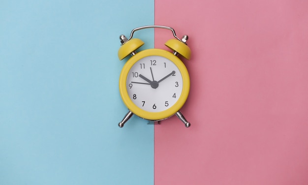 Despertador retro amarelo em fundo rosa azul pastel. . Minimalismo