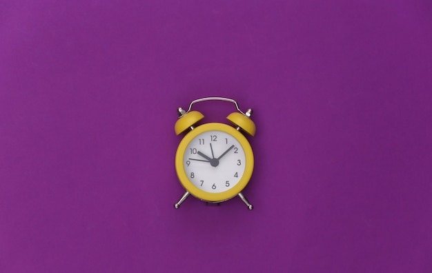 Despertador retrô amarelo sobre fundo roxo. . minimalismo