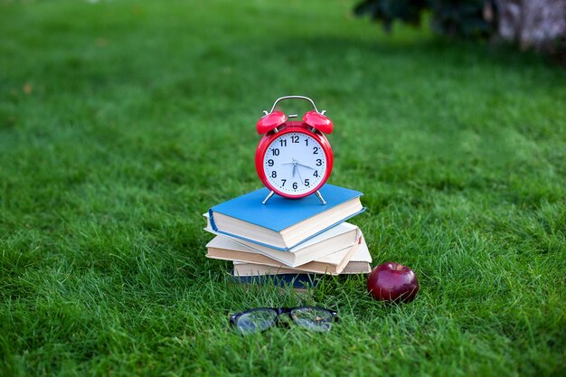 Despertador rojo y apilar libros antiguos en el parque en la mañana de otoño