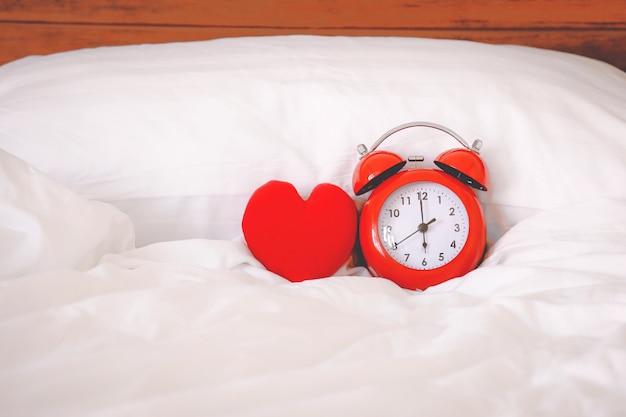 Foto despertador rojo y forma de corazón rojo en la cama en casa