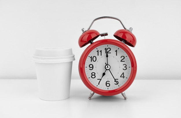 Despertador rojo con taza de café sobre fondo de pared blanca