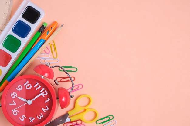 Despertador rojo útiles escolares y artículos de papelería sobre un fondo de color rosa