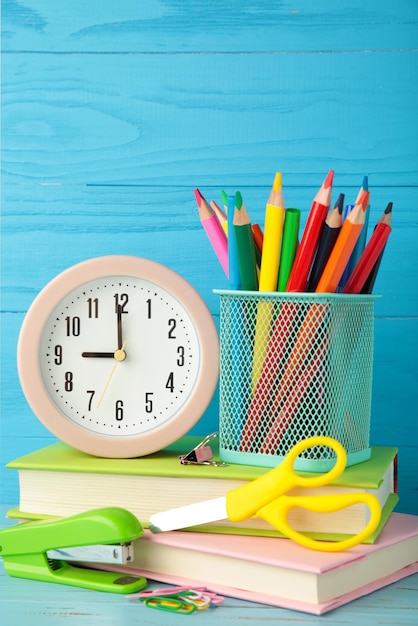 Despertador rosa y accesorios escolares sobre un fondo azul Concepto de regreso a la escuela Foto vertical