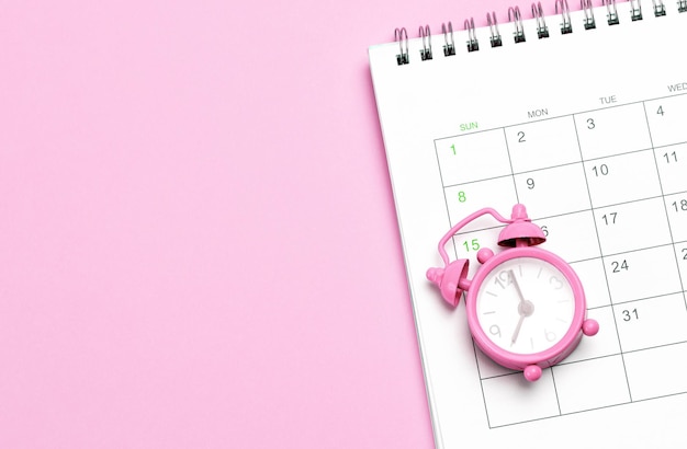 Despertador rosa y calendario sobre un fondo rosa Días conceptuales de menstruación o menopausia Espacio de copia de plantilla para maqueta de texto