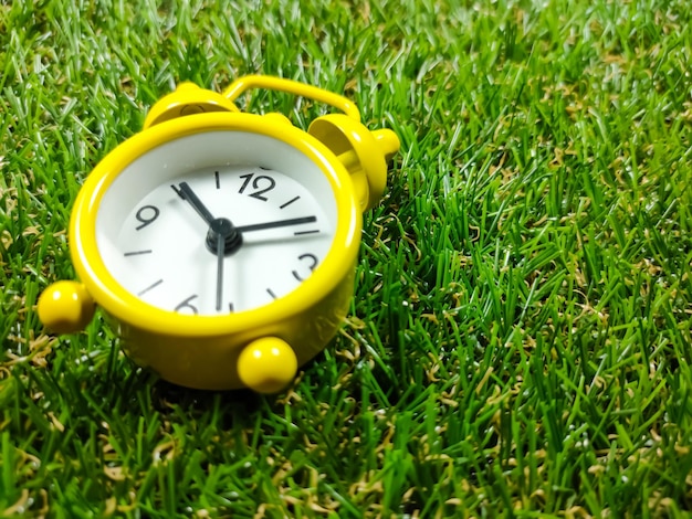 Despertador sobre fondo de hierba Concepto de tiempo Despertador amarillo con hierba verde fresca con espacio de copia