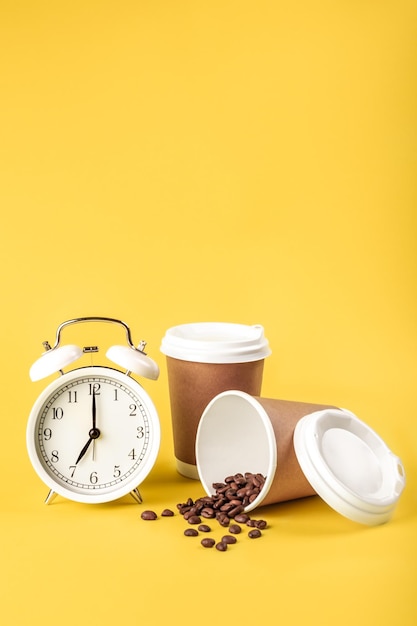 Despertador taza de papel y granos de café sobre un fondo amarillo aislado