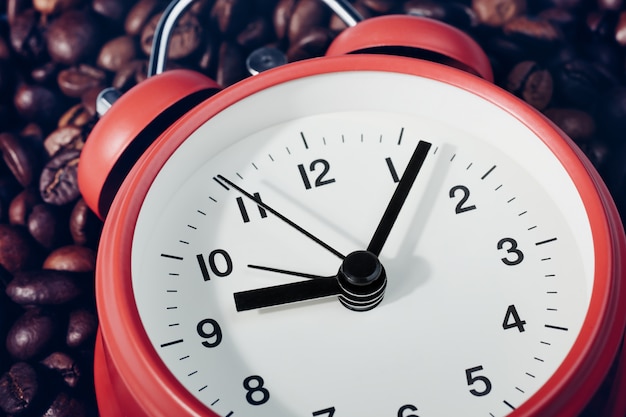 Despertador vermelho deitado sobre grãos de café. Às nove e sete no relógio.